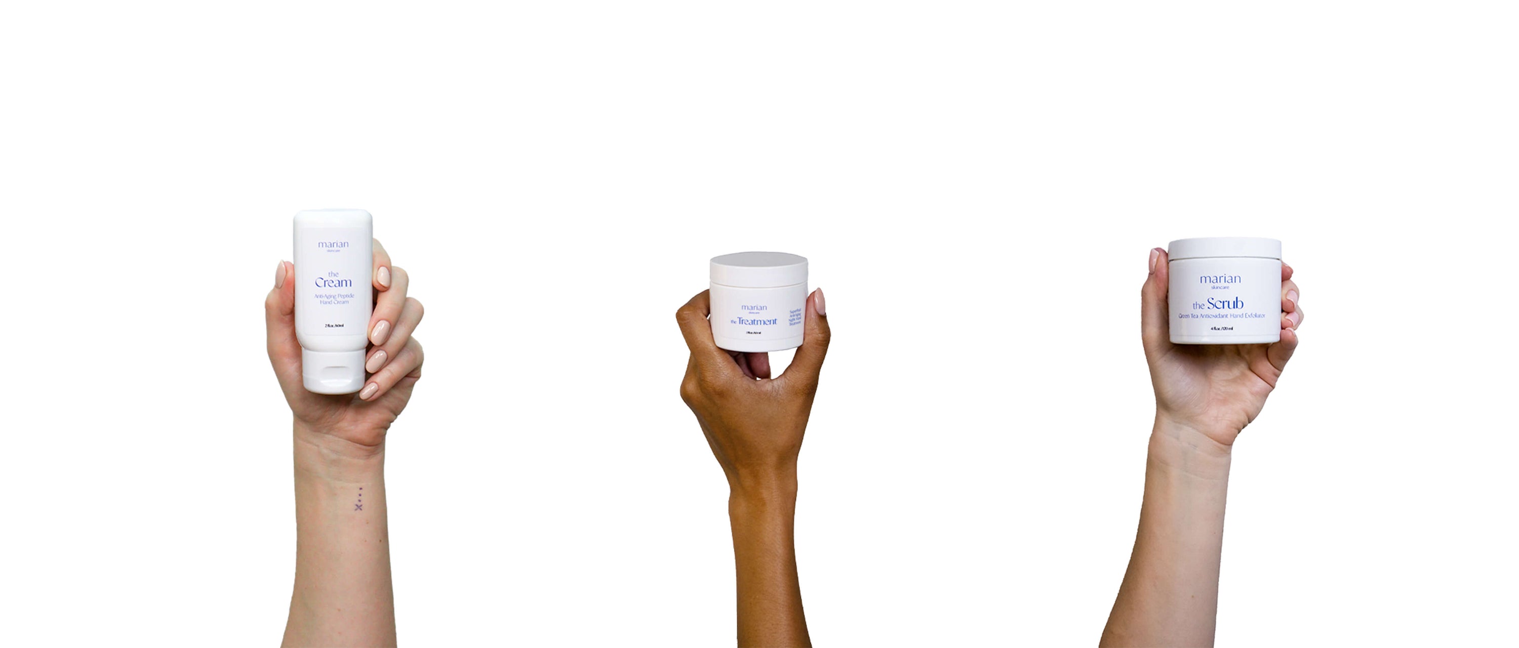 Three hands hold up marian skincare products in white containers with periwinkle lettering. From left: the Cream Anti-Aging Peptide Hand Cream, the Scrub Green Tea Antioxidant Hand Exfoliator, the Treatment Superfruit Anti-Aging Night Hand Treatment.